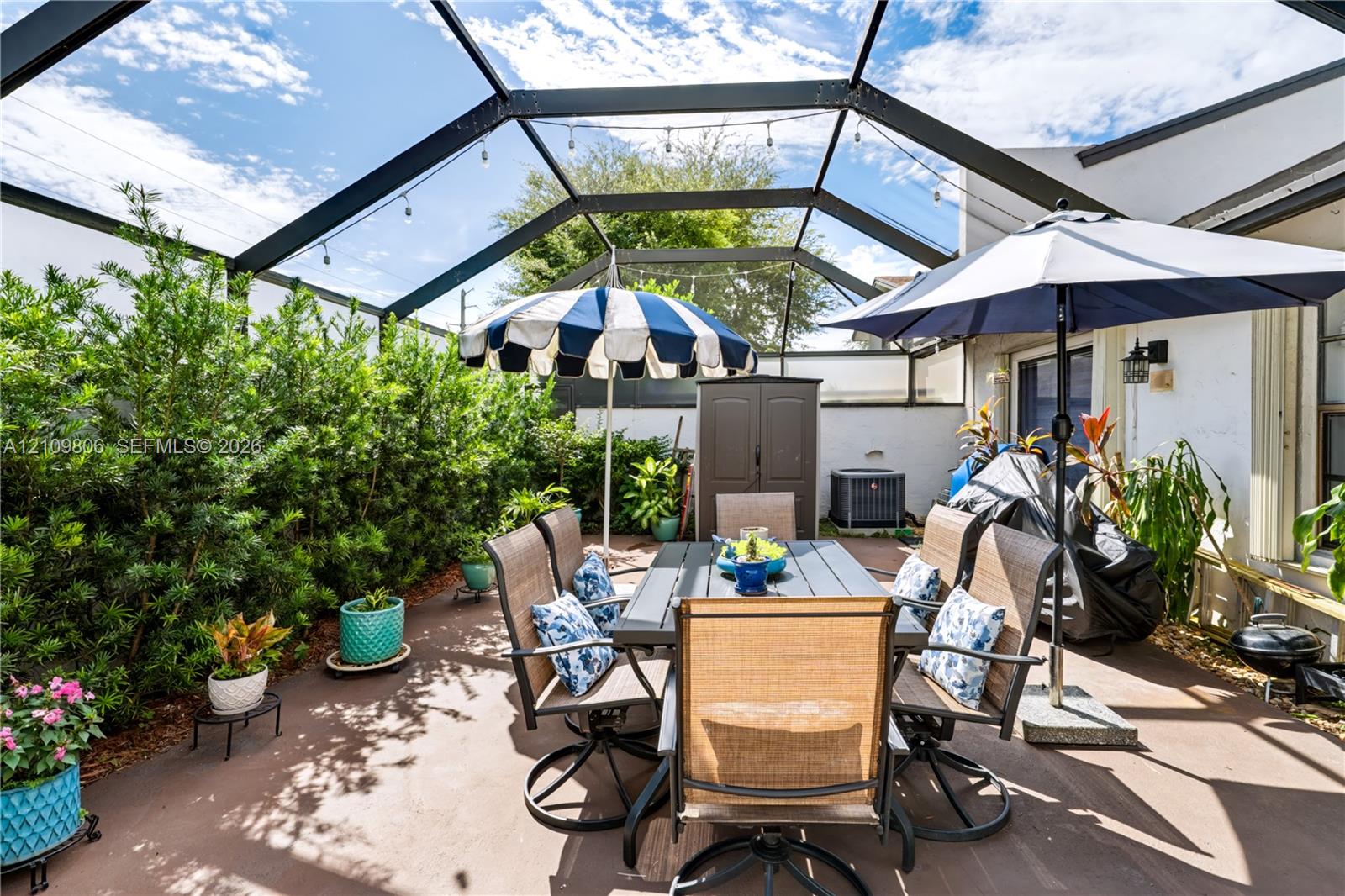 Screened-in patio featuring a concrete floor, privacy hedge, and wall-mounted exterior lighting