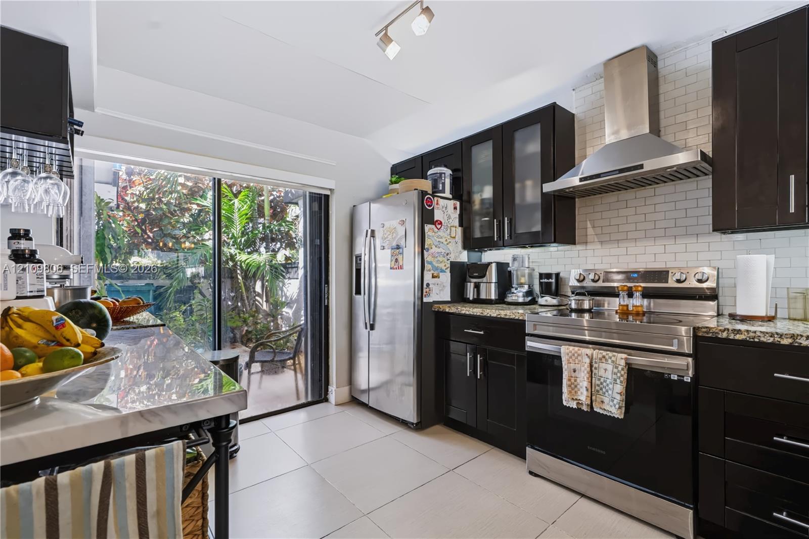Kitchen featuring espresso cabinetry, stone countertops, stainless steel appliances, white subway tile backsplash, and sliding glass doors