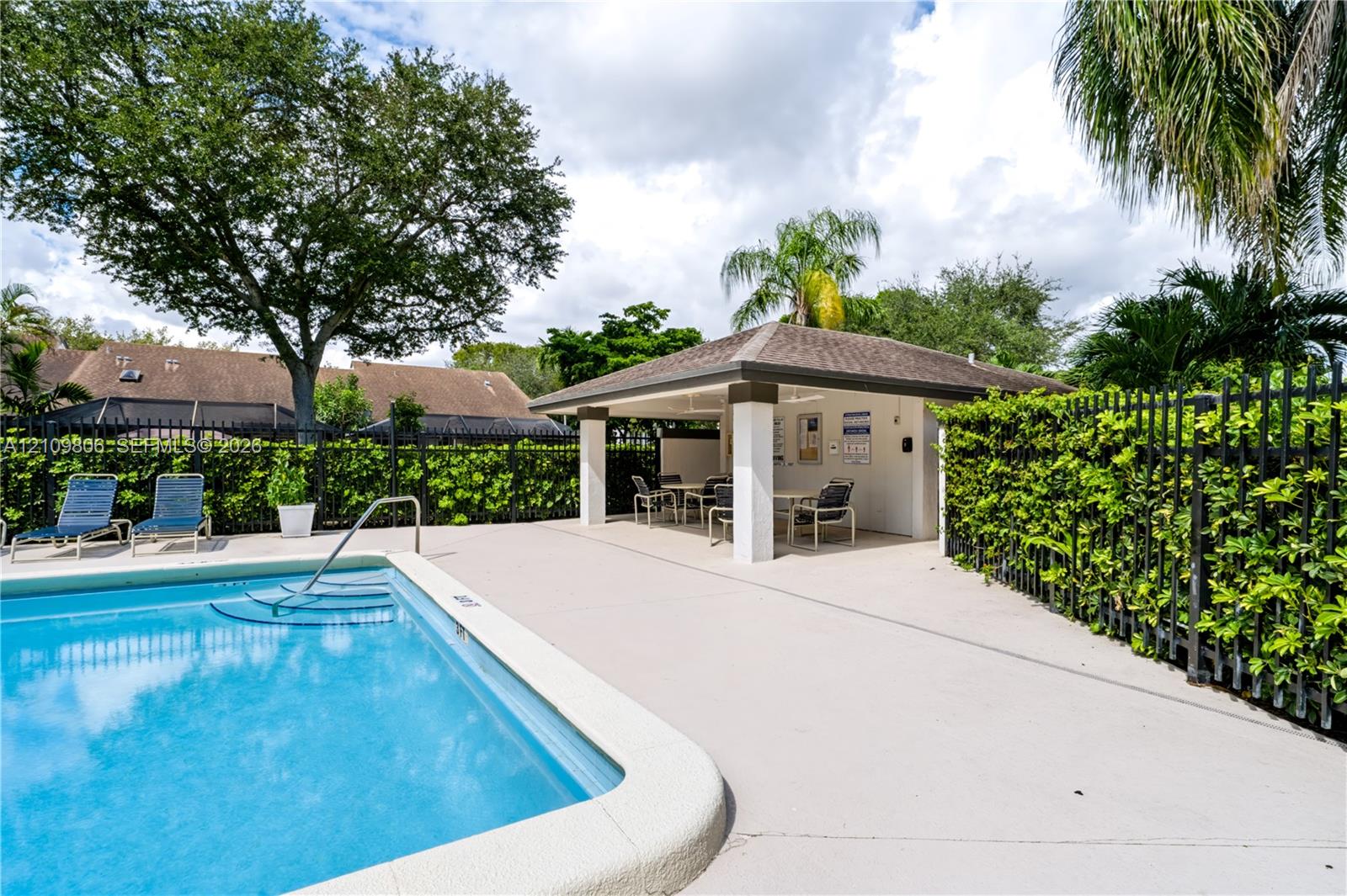 Swimming pool with an integrated metal handrail, expansive concrete deck, and a covered pavilion featuring structural pillars