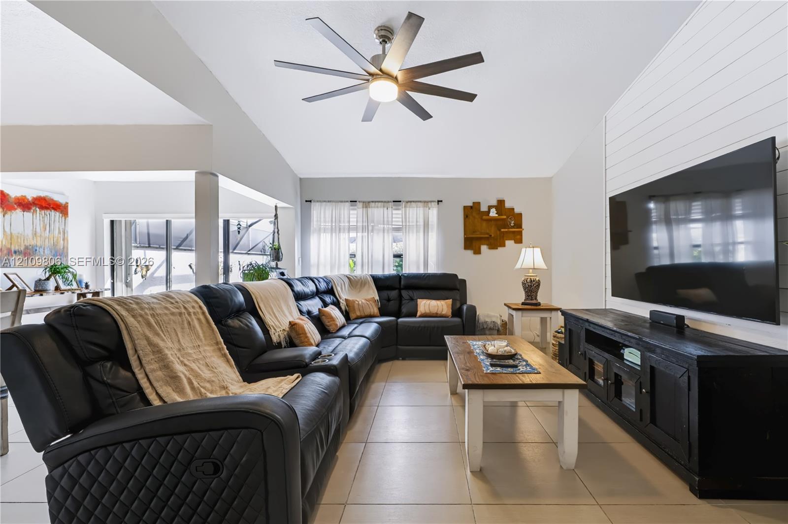 Vaulted ceilings with a multi-blade ceiling fan, light-colored tile flooring, and a white shiplap accent wall