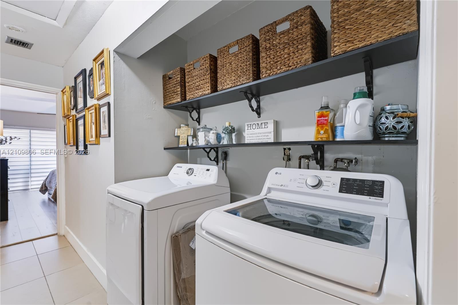 Recessed laundry area featuring two tiered open-shelf storage units with decorative metal brackets and neutral tile flooring