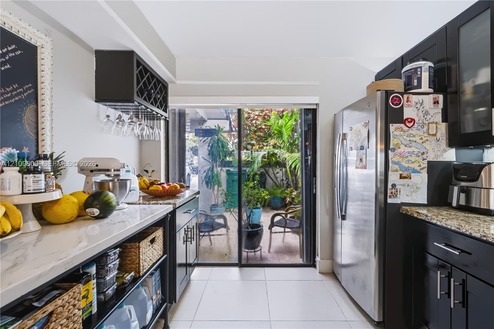 Kitchen featuring dark cabinetry, stone-finish countertops, stainless steel refrigerator, built-in stemware rack, and glass sliding doors