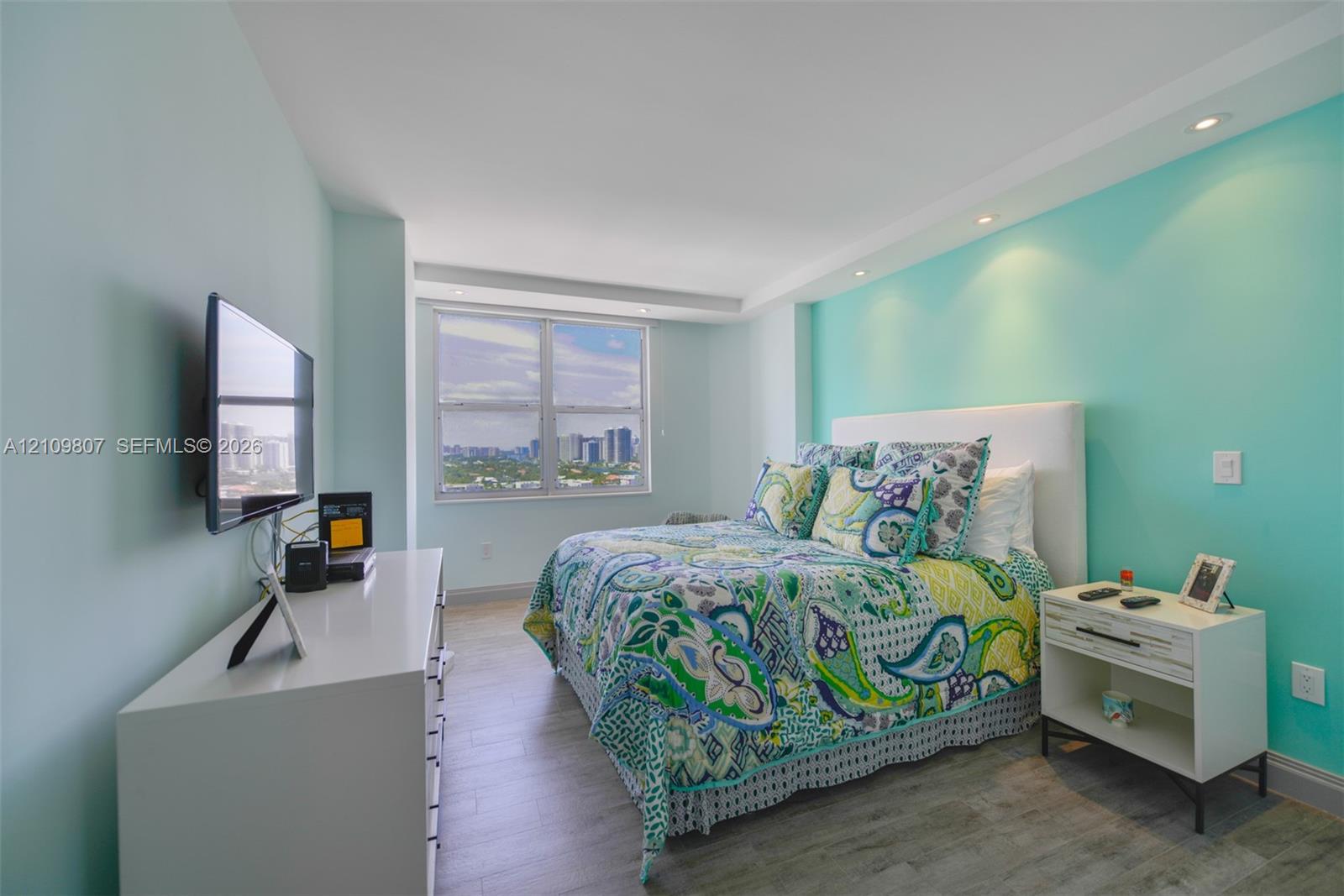 Bedroom featuring wood-finish flooring, recessed ceiling lighting, and a large window with urban scenery