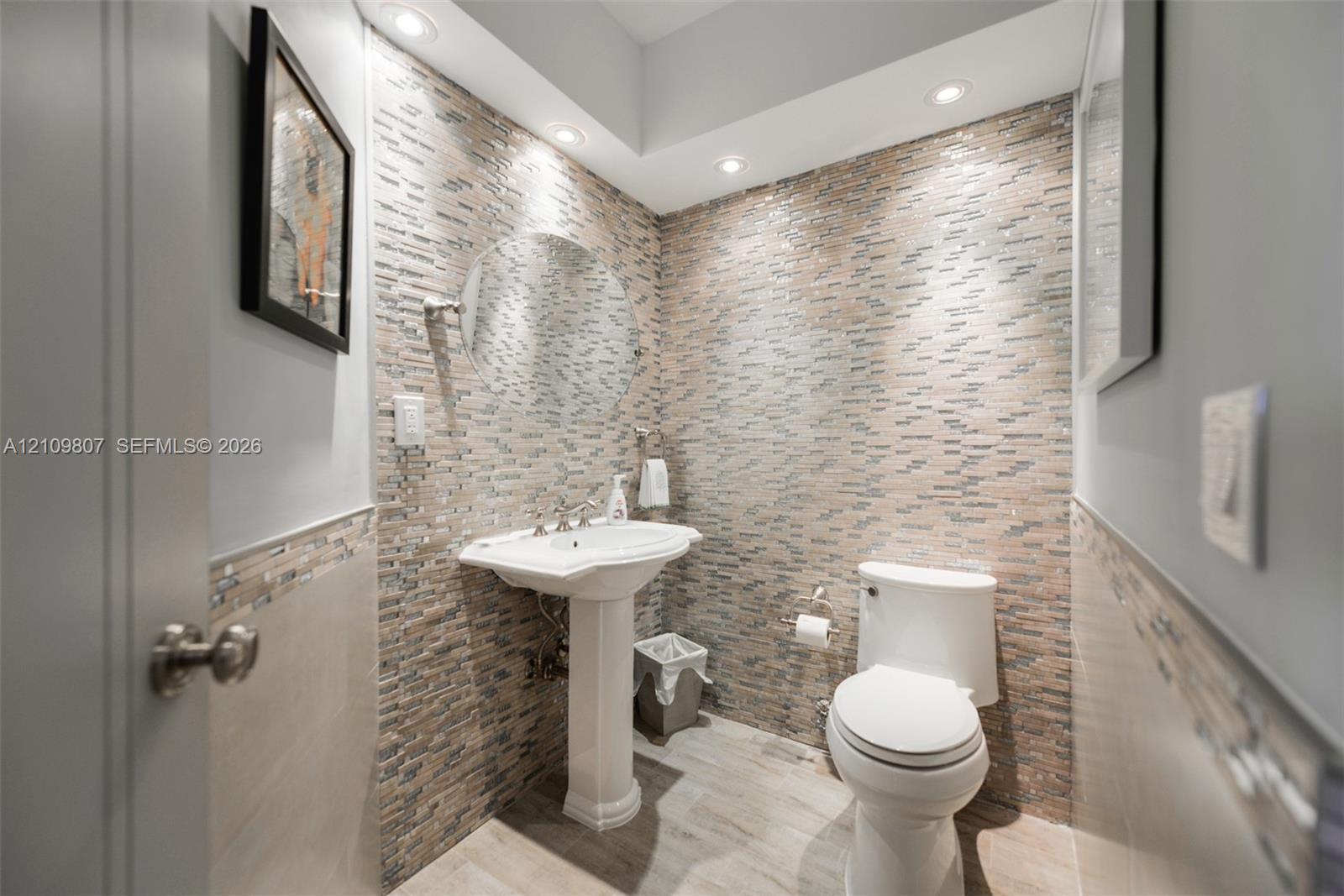 Powder room featuring a stacked-stone accent wall, pedestal sink, recessed lighting, and wood-finish tile flooring