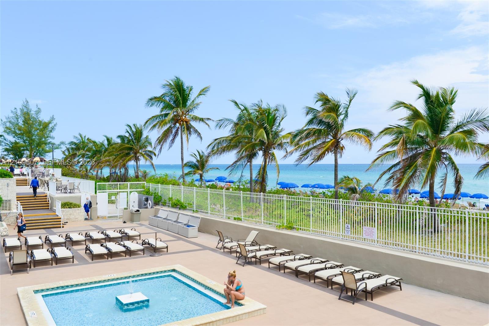 Outdoor pool area featuring a paved deck, tiered steps, and white metal perimeter fencing with ocean frontage