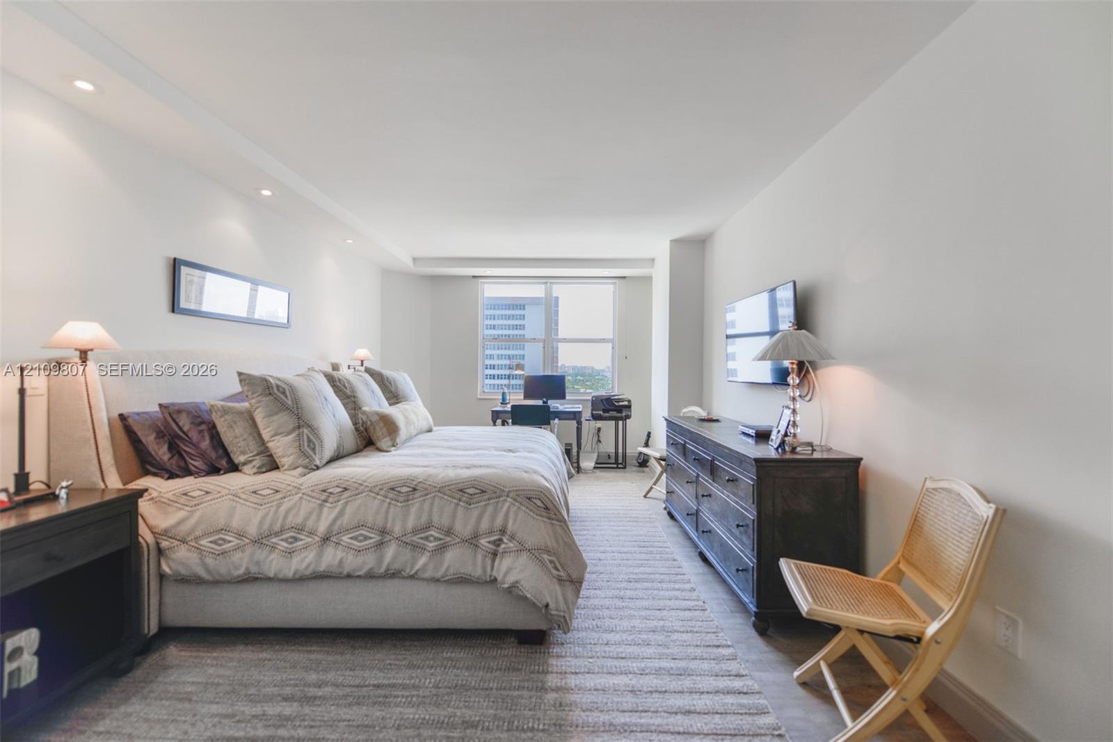 Neutral-toned room featuring recessed ceiling lighting, large-scale window, and wall-mounted television console