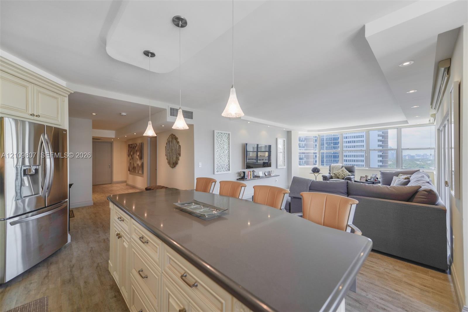 Kitchen island featuring a solid surface countertop, custom cabinetry, stainless steel refrigerator, recessed lighting, and trio of pendant lights
