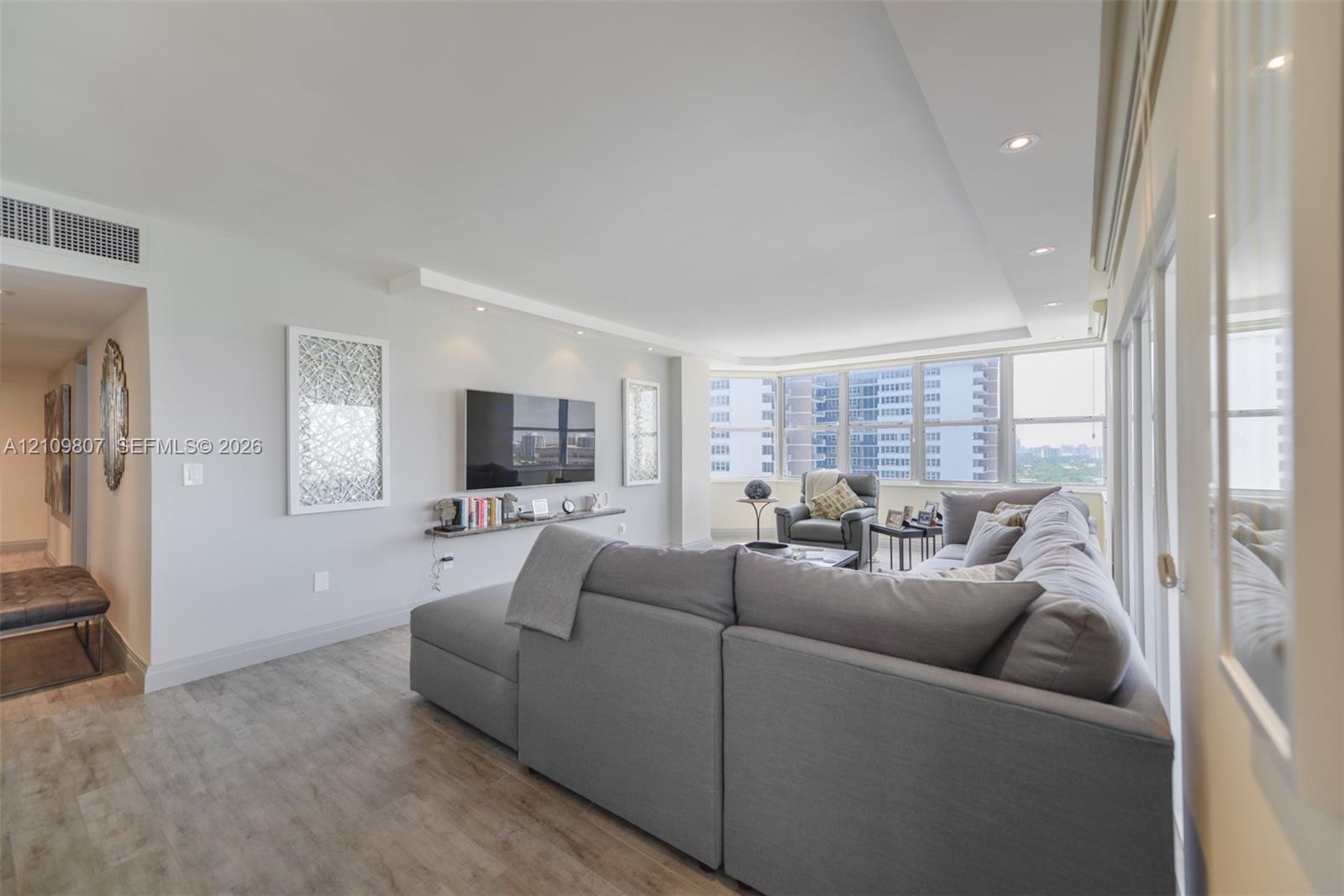Expansive living area featuring wood-finish flooring, recessed lighting, a wall-mounted floating display shelf, and floor-to-ceiling windows