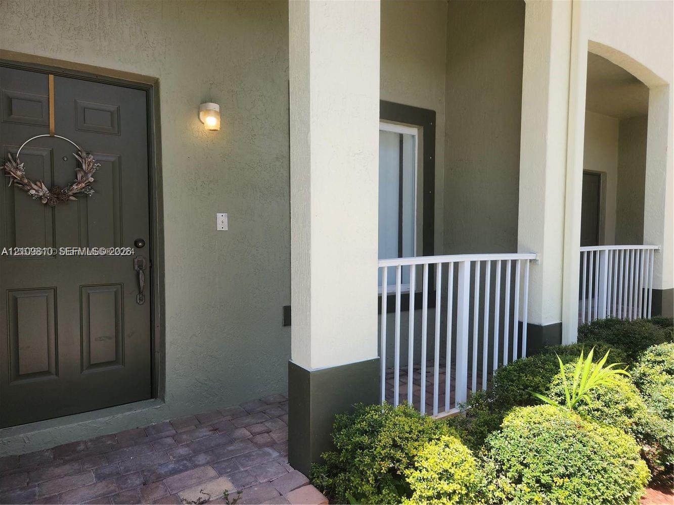 Covered entryway featuring a solid-panel door, square support columns, white metal railing, and paver flooring