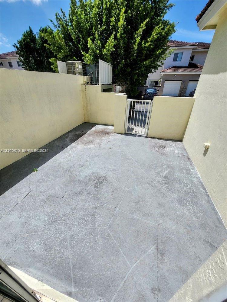Enclosed patio featuring concrete hardscaping, stucco perimeter walls, and a metal security gate
