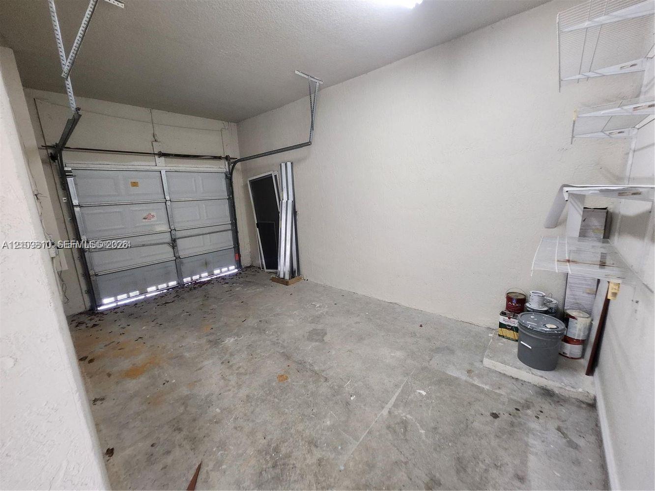 Enclosed garage featuring concrete flooring, a sectional overhead door, and wall-mounted wire shelving