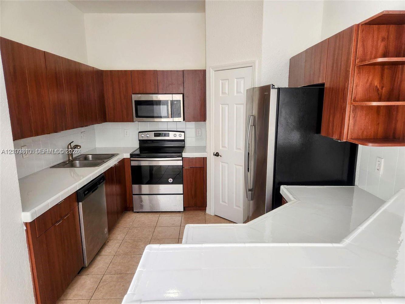 Kitchen featuring wood-finish cabinetry, white tile countertops, stainless steel appliances, and ceramic tile flooring
