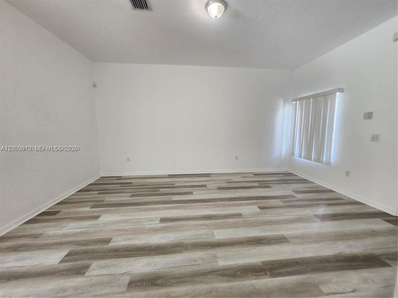 Interior space featuring wood-finish flooring, white walls, and vertical window blinds