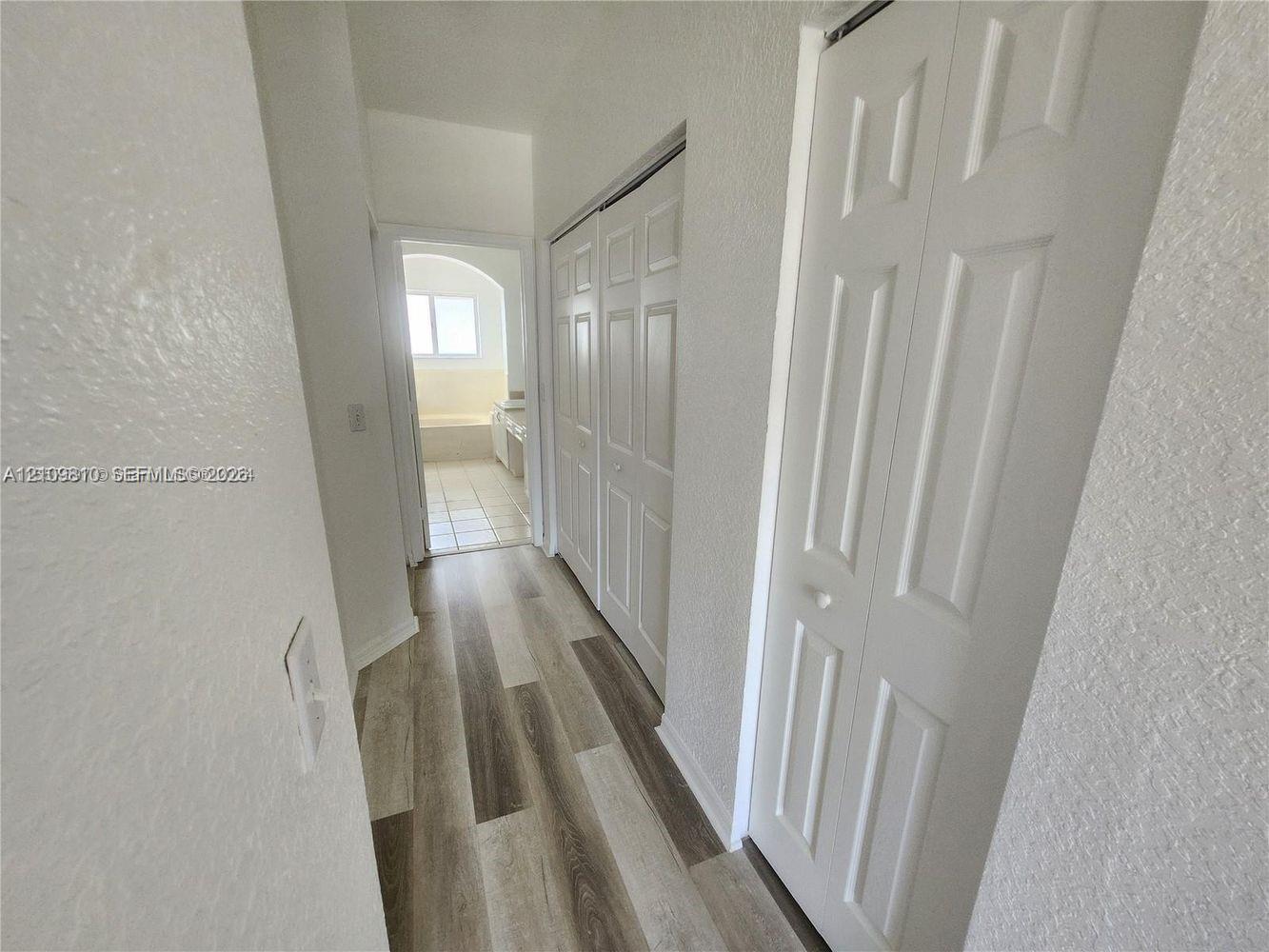 Hallway featuring wood-finish plank flooring and dual sets of bi-fold closet doors