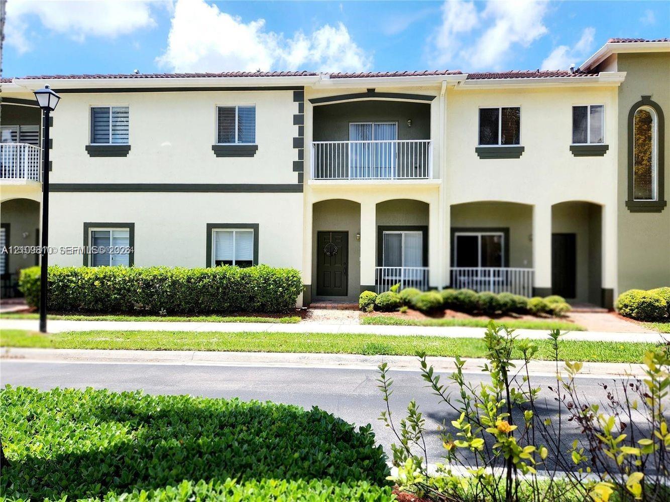Two-story exterior featuring light-toned stucco walls with contrasting trim, a tiled roof, a private upper-level balcony with white railings, and covered lower-level entryways