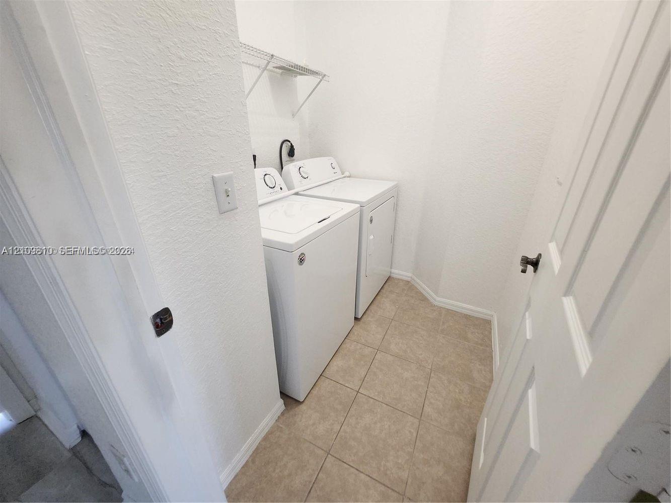 Laundry area featuring ceramic tile flooring, white-finish appliances, and built-in wire shelving