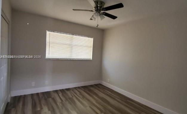 Neutral-toned interior space featuring wood-finish flooring, a ceiling fan with integrated lighting, and a single-panel interior door