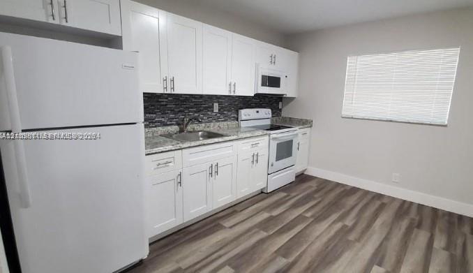 Kitchen featuring white shaker-style cabinetry, stone-finish countertops, decorative tile backsplash, integrated white appliances, and wood-finish flooring