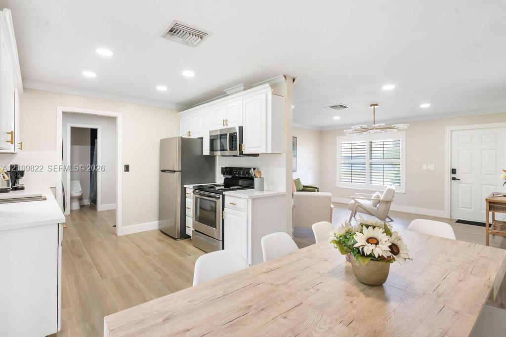 Kitchen featuring white cabinetry, stainless steel appliances, wood-finish flooring, recessed lighting, and a multi-light chandelier
