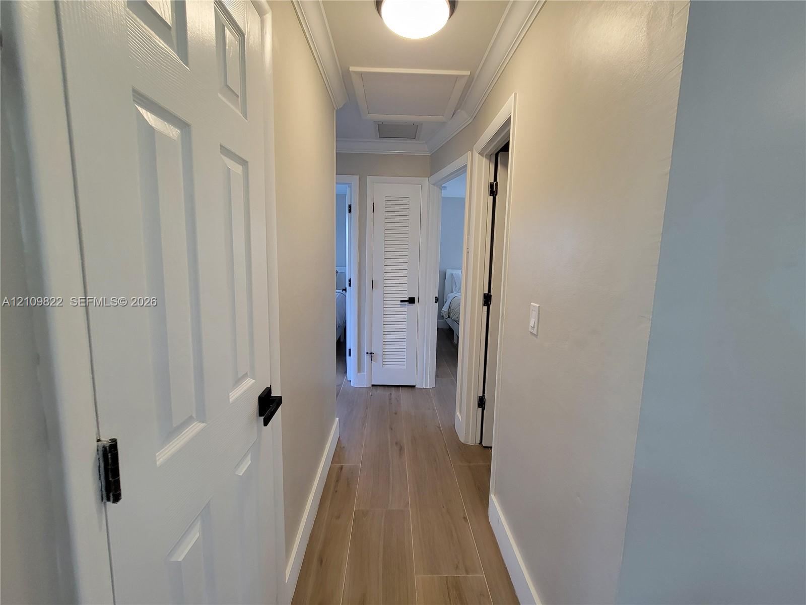 Hallway featuring wood-finish flooring, crown molding, multi-panel doors with matte black hardware, and a louvered closet door