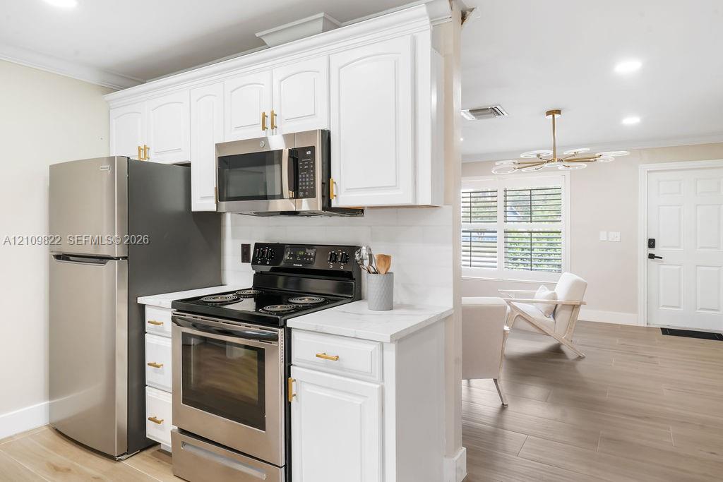 Kitchen featuring white shaker-style cabinetry, stainless steel appliances, stone-look countertops, and wood-finish flooring
