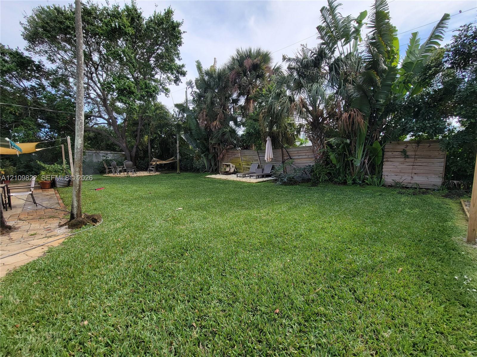 Expansive backyard featuring a natural grass lawn, mature palm trees, flagstone patio, and perimeter wood fencing