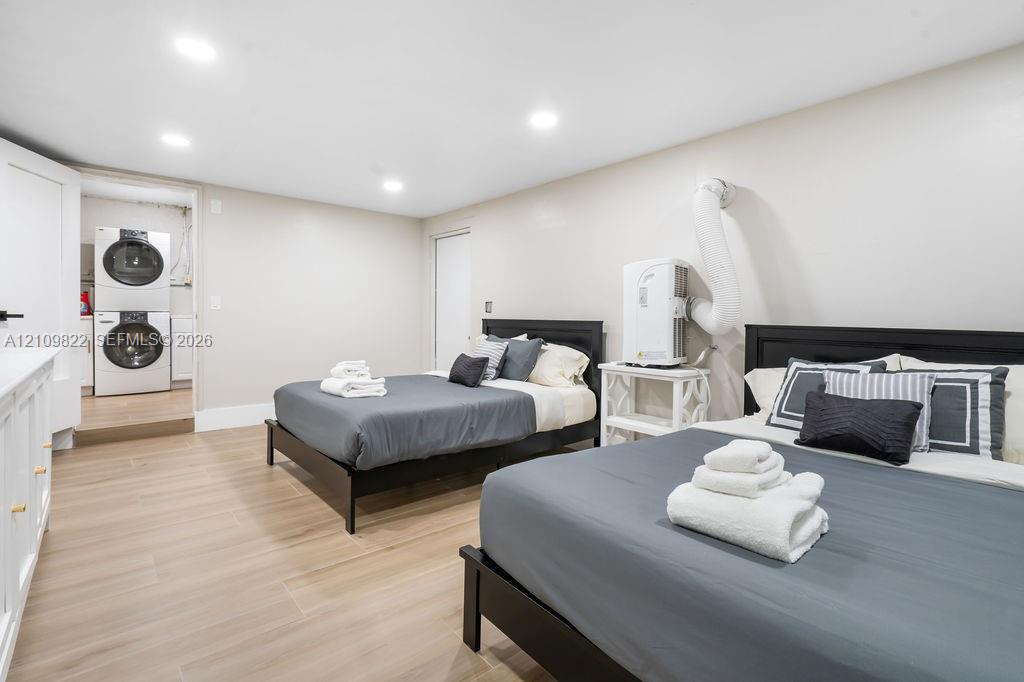 Neutral-toned room featuring wood-finish flooring, recessed lighting, and a laundry closet equipped with a stacked washer and dryer