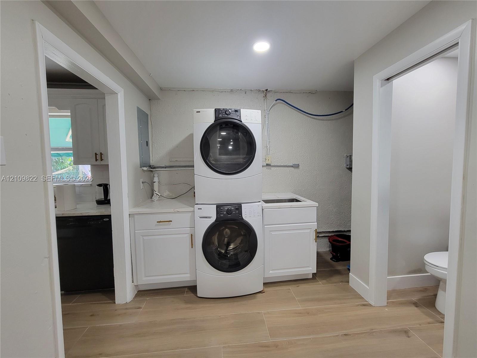 Utility area featuring white shaker-style cabinetry, an integrated sink with a countertop, and wood-finish tile flooring
