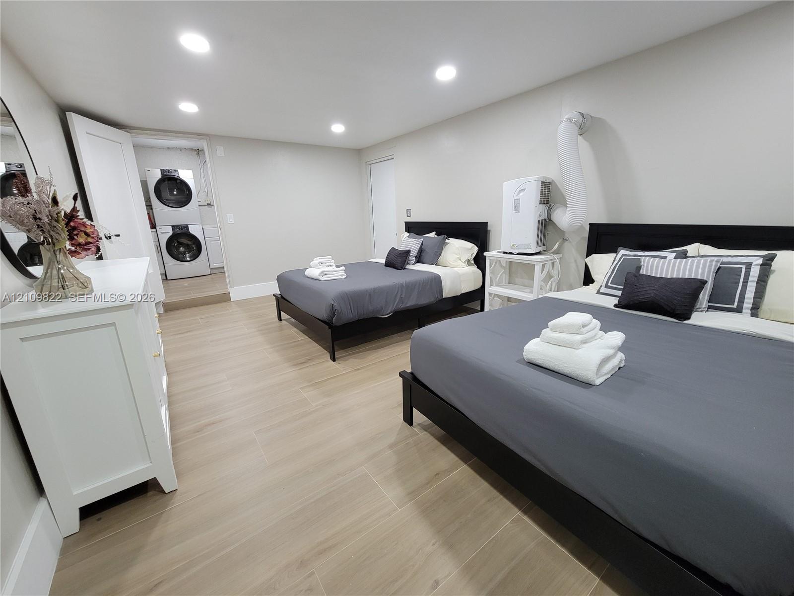 Neutral-toned interior space featuring light wood-finish flooring, recessed lighting, and a dedicated laundry area with stacked washer and dryer unit