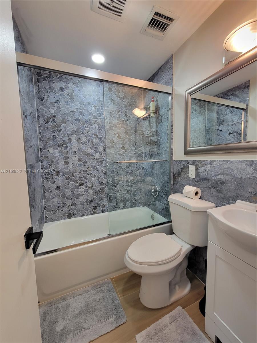 Bathroom featuring a shower-tub combination with sliding glass doors, hexagon-patterned tile surround, vanity with an integrated basin, and framed wall mirror