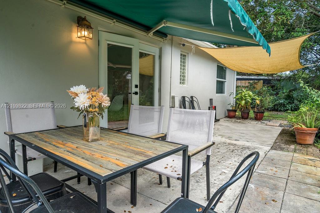 Concrete patio featuring a retractable green awning, overhead shade sail, wall-mounted lantern lighting, and glass-paneled double doors