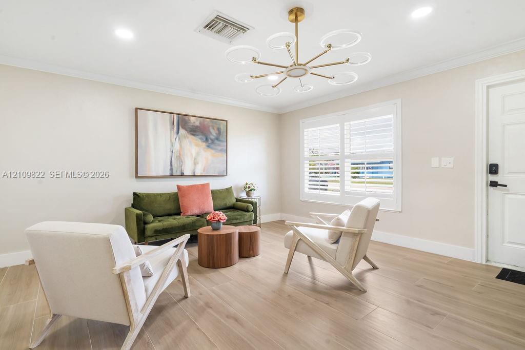 Living area featuring wood-finish flooring, a contemporary multi-light chandelier, crown molding, and plantation shutters