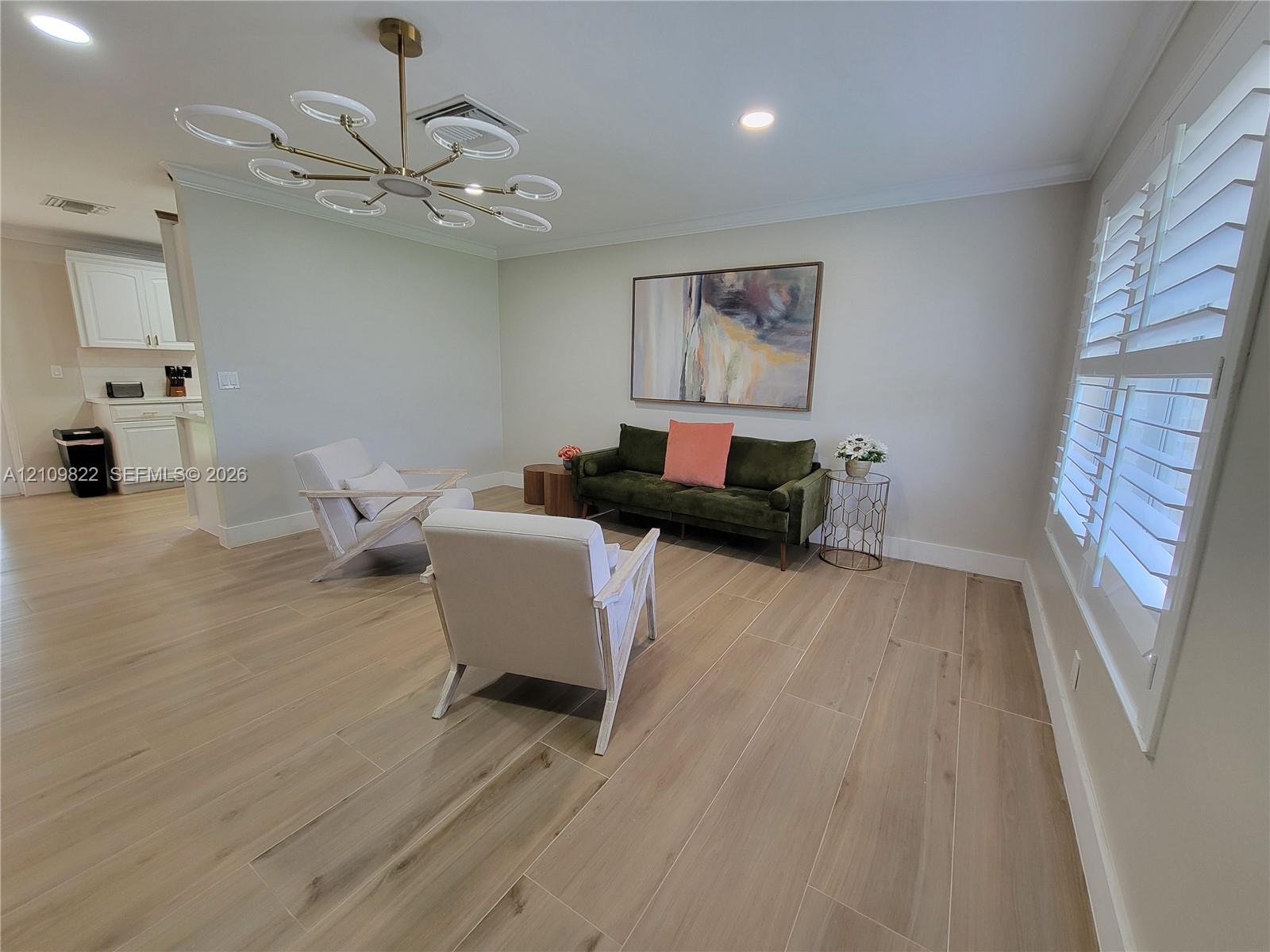 Wood-finish flooring, contemporary multi-ring chandelier, recessed lighting, and white plantation shutters
