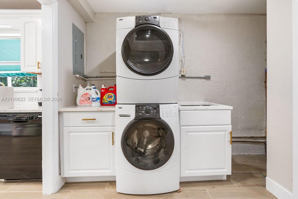 Laundry area featuring a stacked washer and dryer, white shaker-style cabinetry, and a countertop with an integrated basin