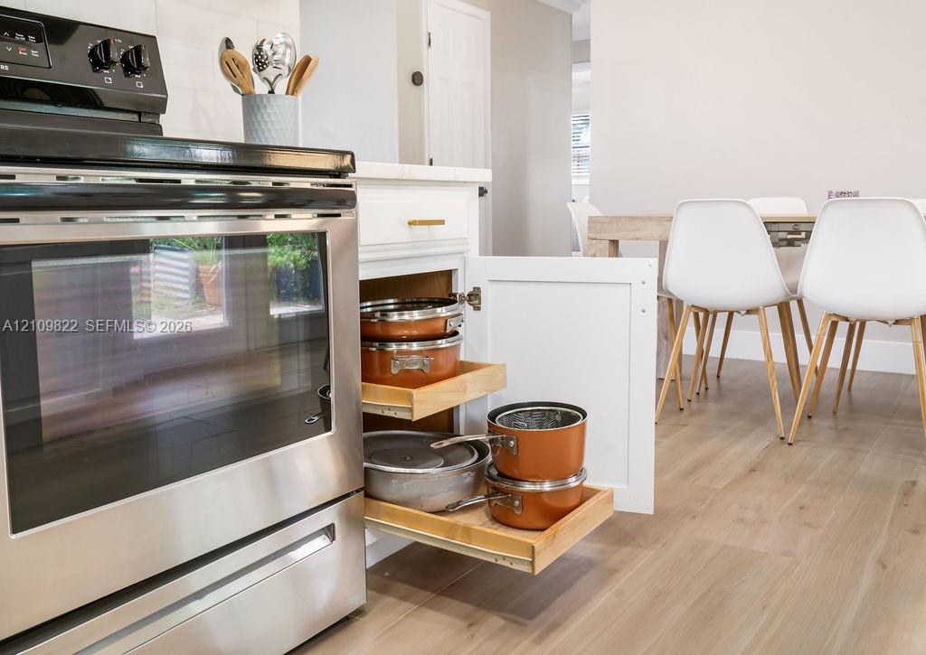 Kitchen featuring stainless steel range, custom white cabinetry with pull-out shelving, and wood-finish flooring