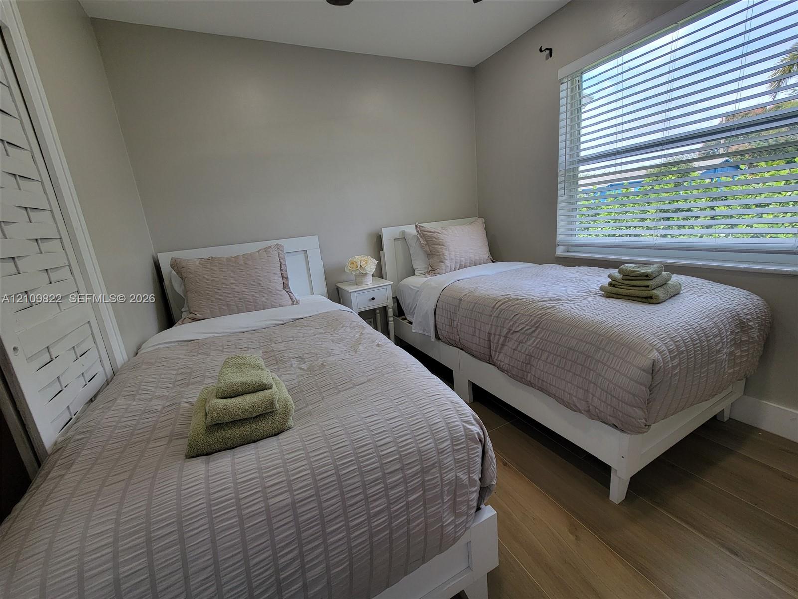 Neutral-toned interior space featuring wood-finish flooring, a large window with horizontal blinds, and a closet with louvered double doors