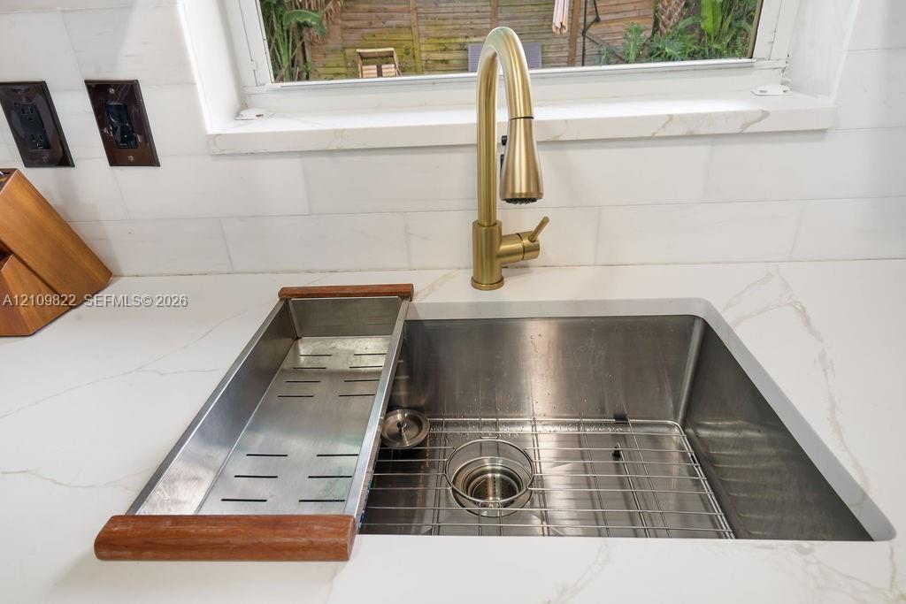 Undermount stainless steel kitchen sink featuring a brass high-arc pull-down faucet, stone-finish countertops, and subway-tile backsplash