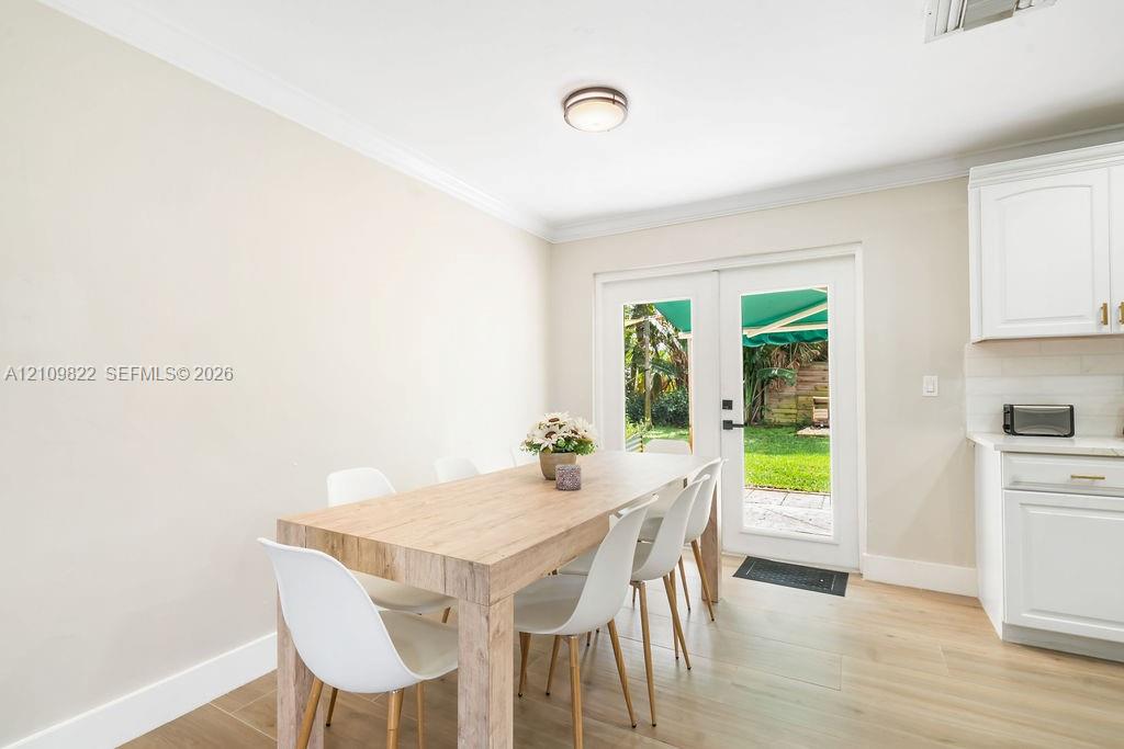 Neutral-toned room featuring wood-finish flooring, white Shaker-style cabinetry, crown molding, and double glass-paneled exterior doors