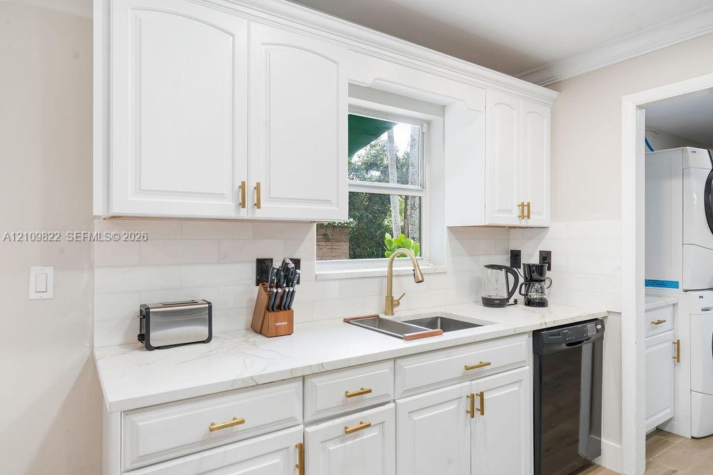 Kitchen featuring white cabinetry, light-toned stone-finish countertops, brass-toned hardware, subway tile backsplash, and an undermount sink with a matching pull-down faucet
