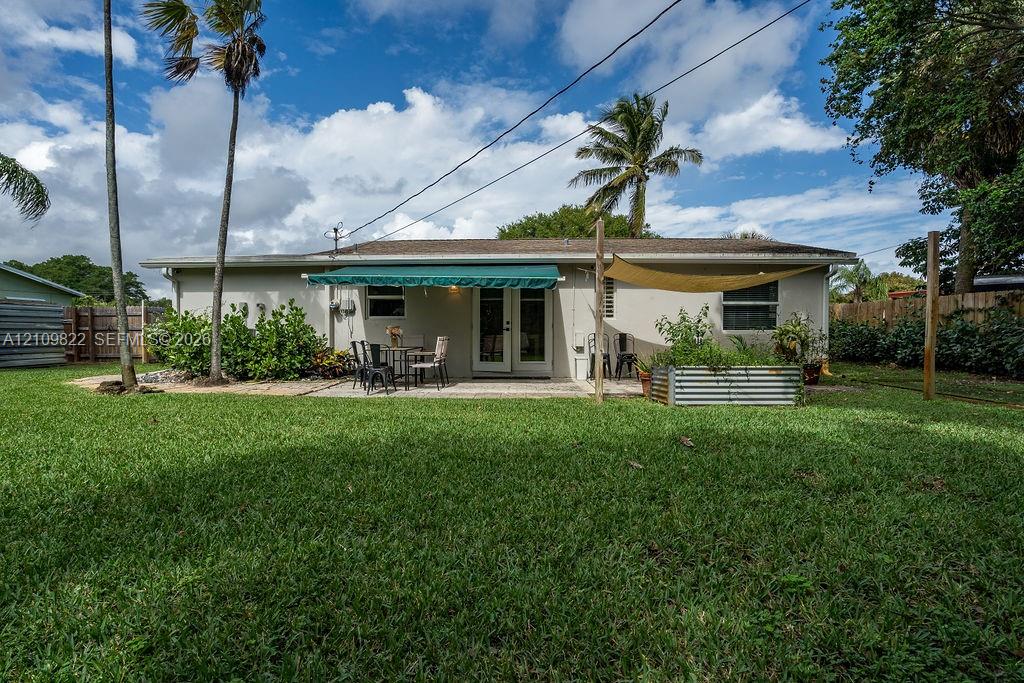 Expansive backyard featuring a manicured lawn, paved patio, retractable awning, mature palms, and metal raised garden beds