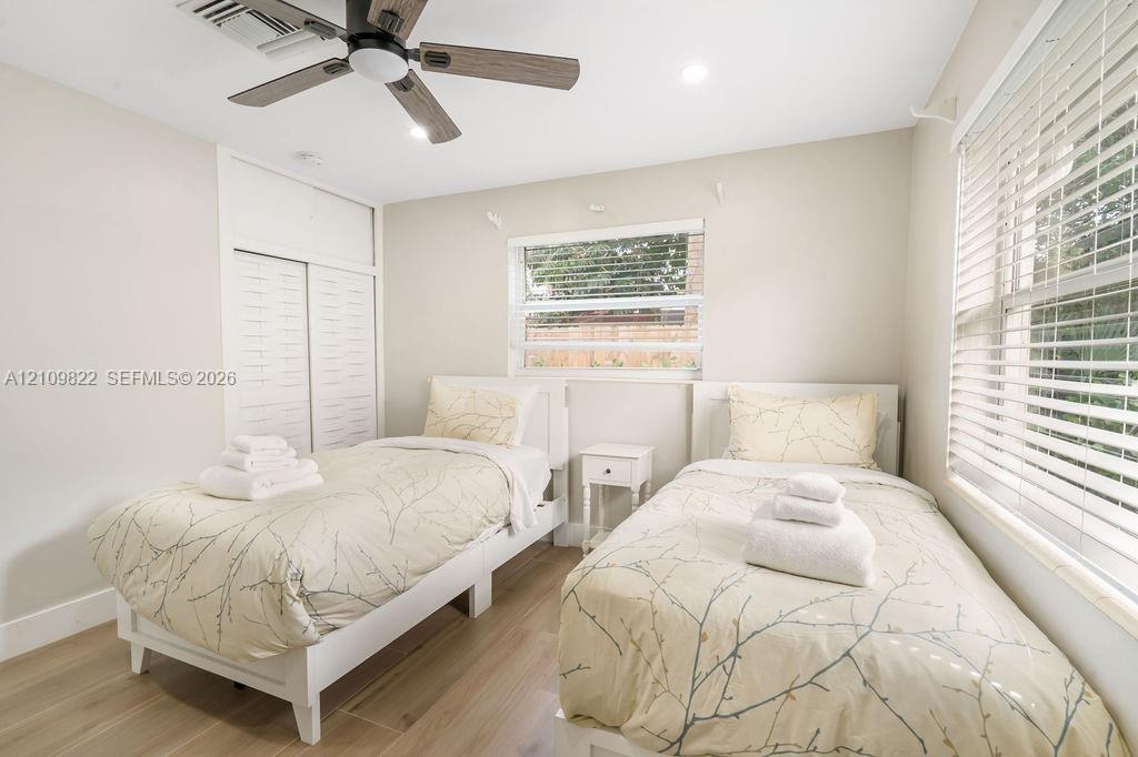 Neutral-toned interior featuring wood-finish flooring, a multi-blade ceiling fan, recessed lighting, and dual-window installations with horizontal blinds