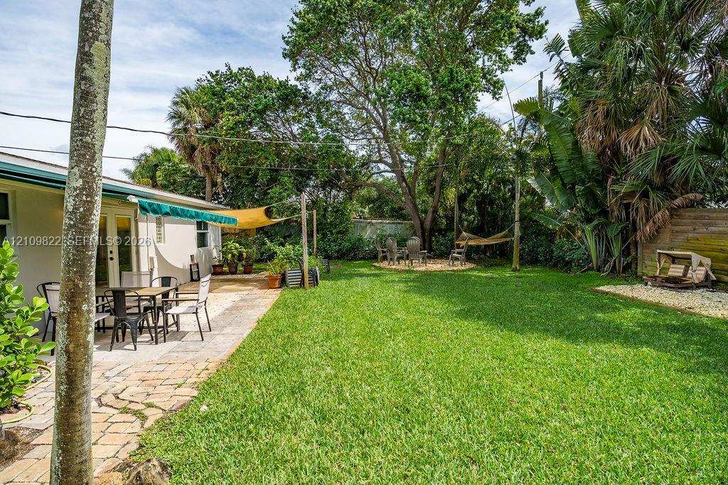 Backyard featuring a paved stone patio, mature canopy trees, lush lawn, and palm-lined perimeter