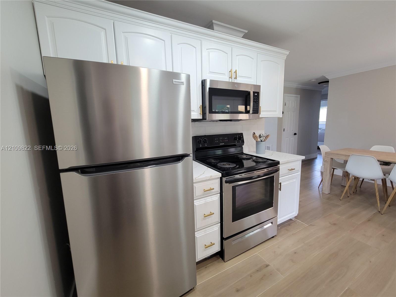 Kitchen featuring white shaker-style cabinetry with gold-toned hardware, stainless steel appliances, stone-finish countertops, and wood-finish flooring