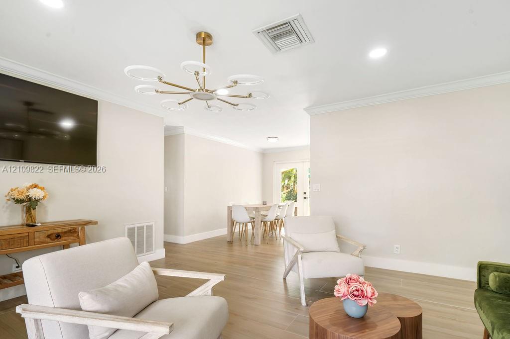 Modern multi-arm ring chandelier, recessed lighting, crown molding, and continuous wood-finish flooring
