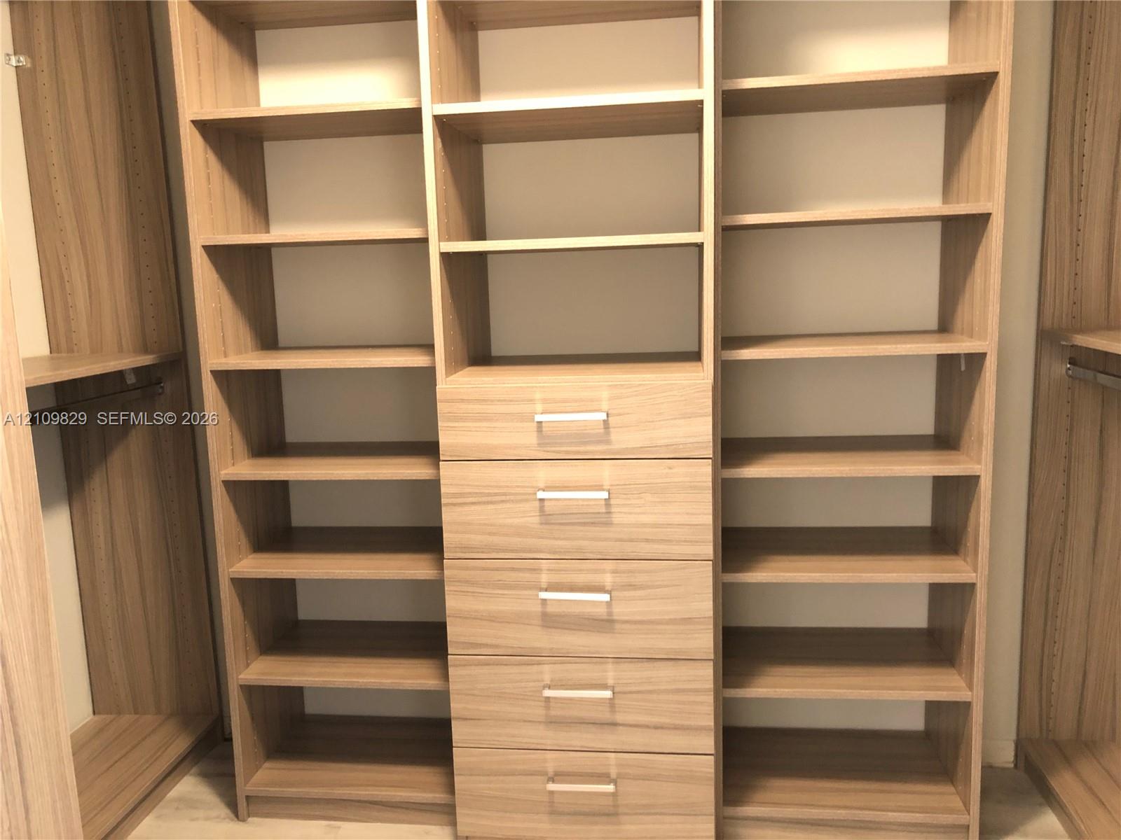 Customized storage system featuring wood-finish cabinetry, adjustable shelving, integrated drawer stack, and horizontal metallic pulls