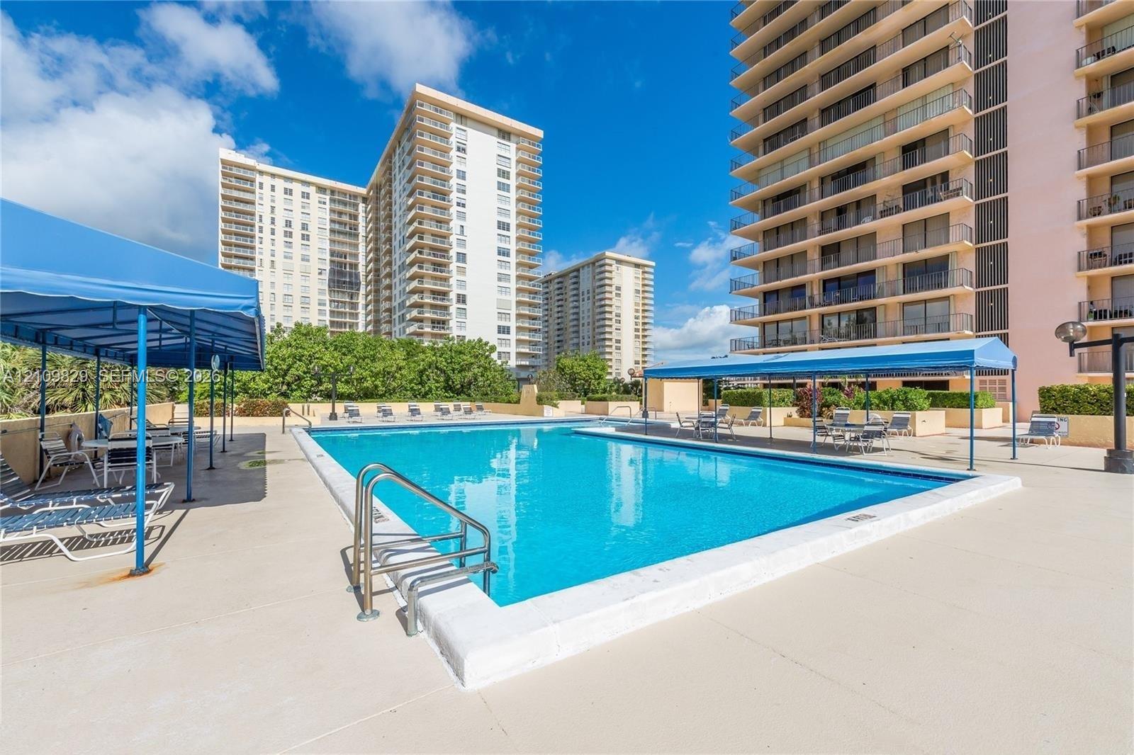 Swimming pool featuring a concrete deck, metal railings, and dual blue-fabric awnings