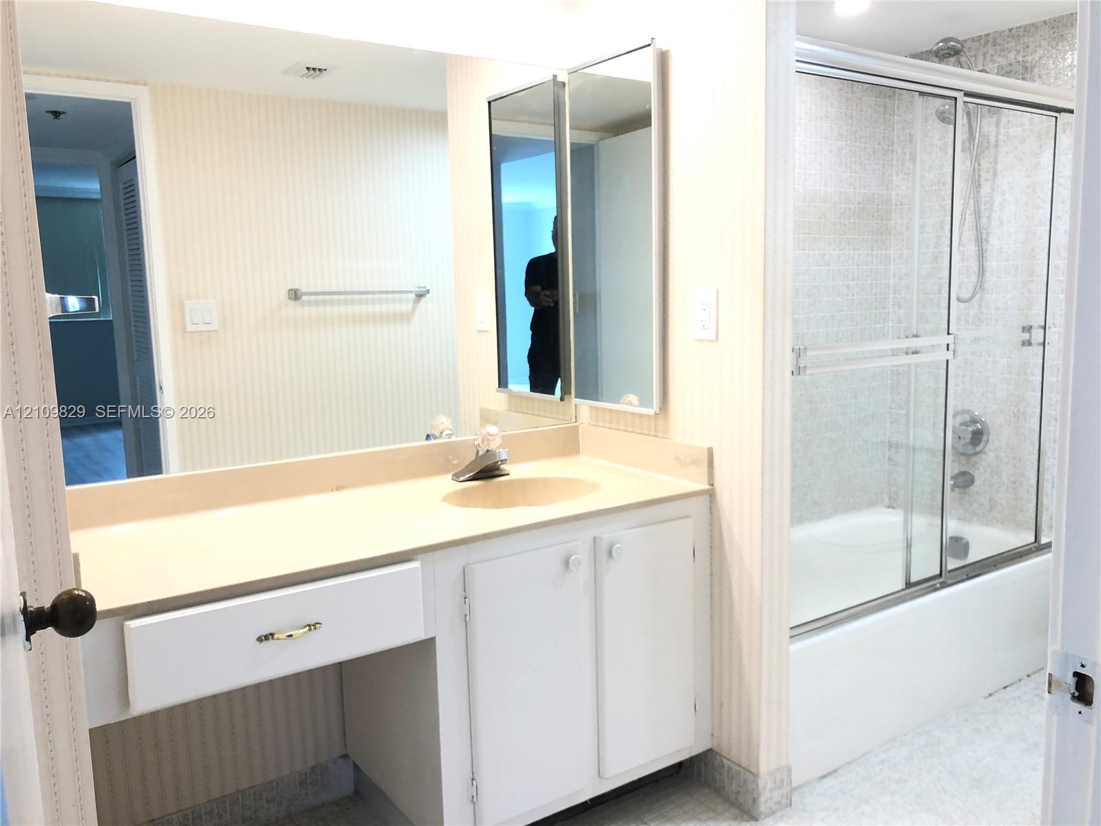 Bathroom featuring a single-sink vanity with solid-surface countertop, full-width wall mirror, medicine cabinet, and a tiled shower-tub combination with sliding glass doors