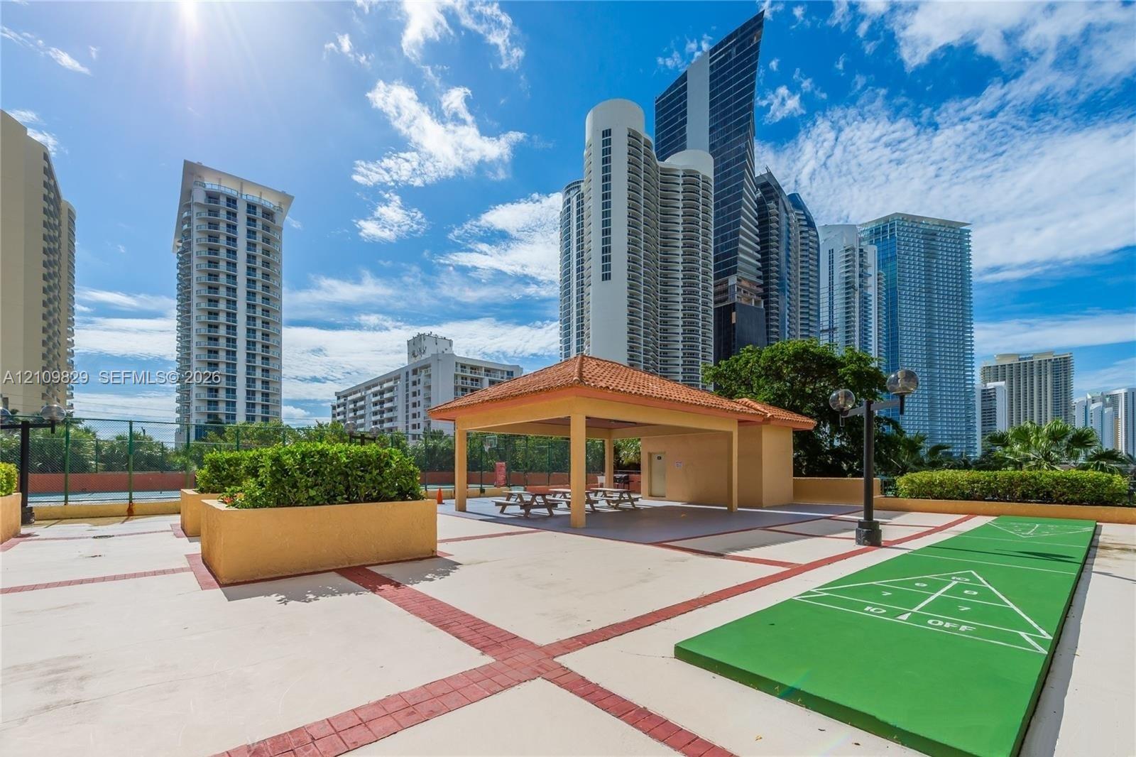 Outdoor terrace featuring a concrete deck with masonry accents, a covered pavilion with a terracotta-style roof, and a built-in shuffleboard court