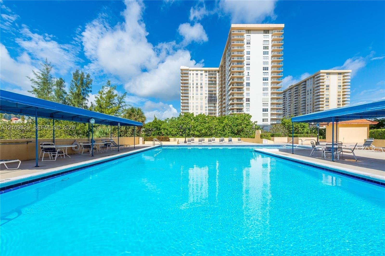 Rectangular swimming pool featuring tiled coping, dual shaded lounge areas with metal frame coverings, and concrete decking