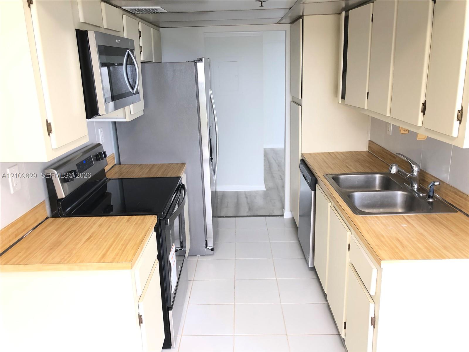 Kitchen featuring white cabinetry, light-toned wood-finish countertops, stainless steel appliances, and tile flooring